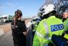 Enforcement, police and licensing officers stand in the layby of a busy A-road, ready to pull vehicles over for inspection. The enforcement officer is talking on a radio device. 